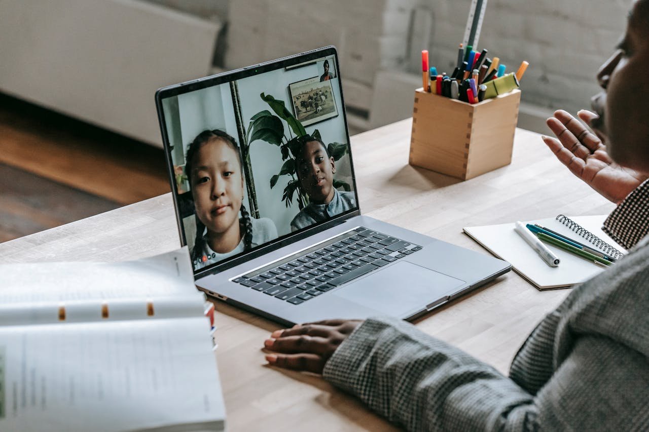 From above of crop confident African American female teacher sitting in classroom and teaching multiethnic pupils remotely on laptop during coronavirus pandemic